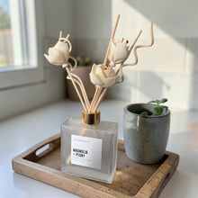Load image into Gallery viewer, JD Candle Co. 6.7 oz frosted Reed Diffuser square bottle with floral reeds on a wooden tray next to a small plant, in a bright room.