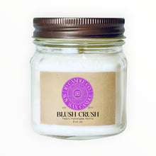 Load image into Gallery viewer, JD Candle Co. Blush Crush 8 oz soy wax candle in a clear mason jar with a bronze lid. Features a kraft paper label with purple logo and scent notes of peach, hydrangea, and vanilla.